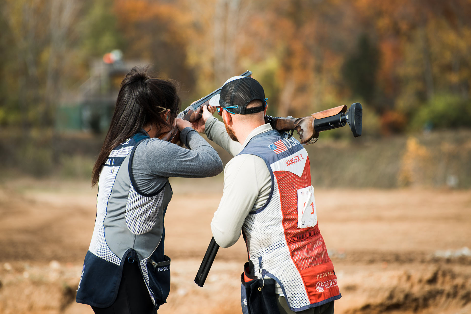 Female athlete aiming shotgun receiving assistance from shooting instructor.