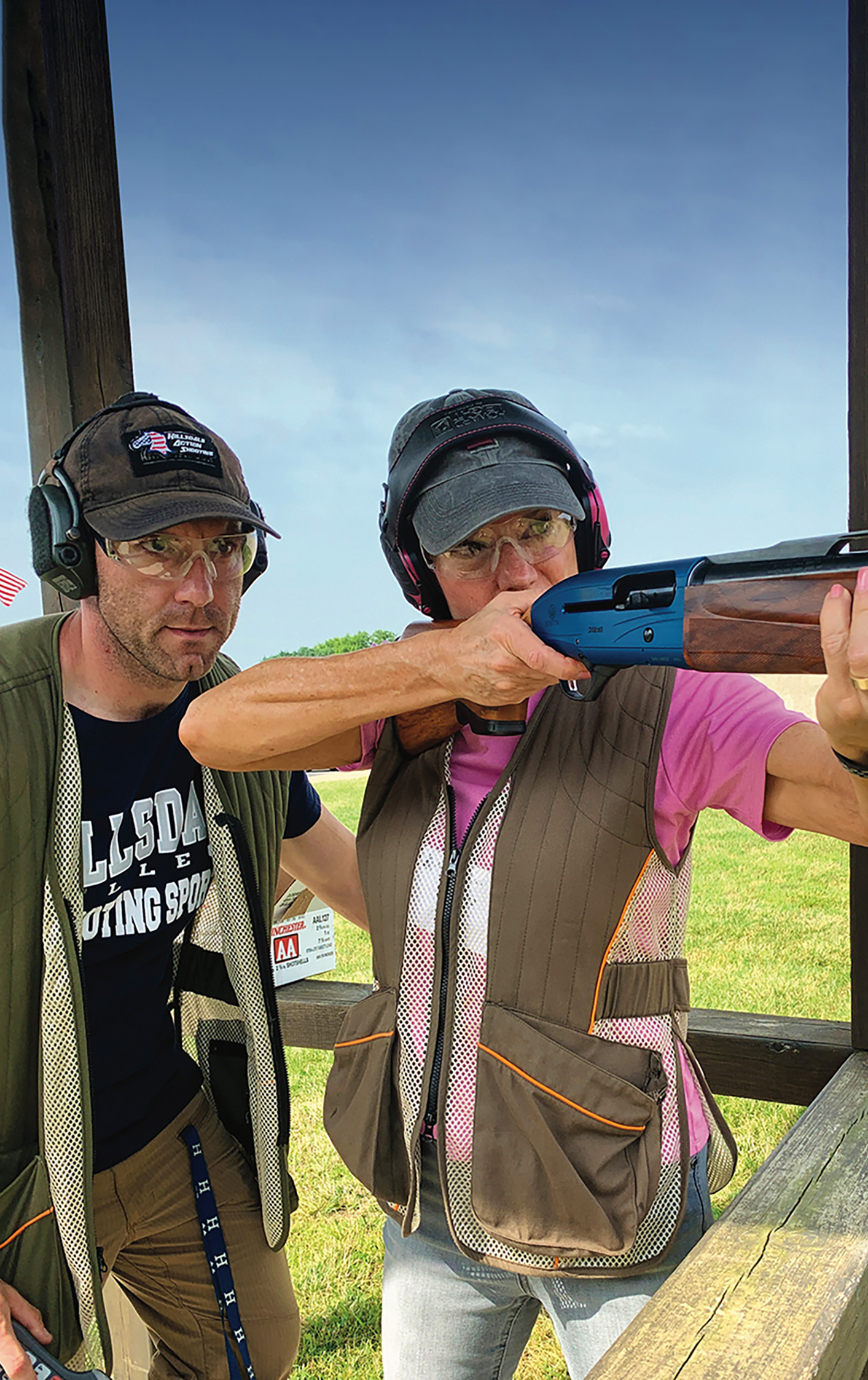 Female aiming a shotgun with a male instructor standing nearby.