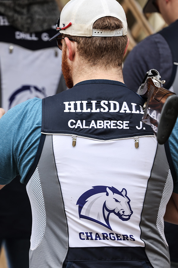 cropped vertical picture of man with back to camera with Hillsdale College and Charger horse logo on vest