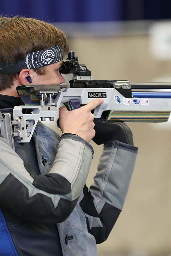 Youth boy with air rifle aims down range while wearing head band
