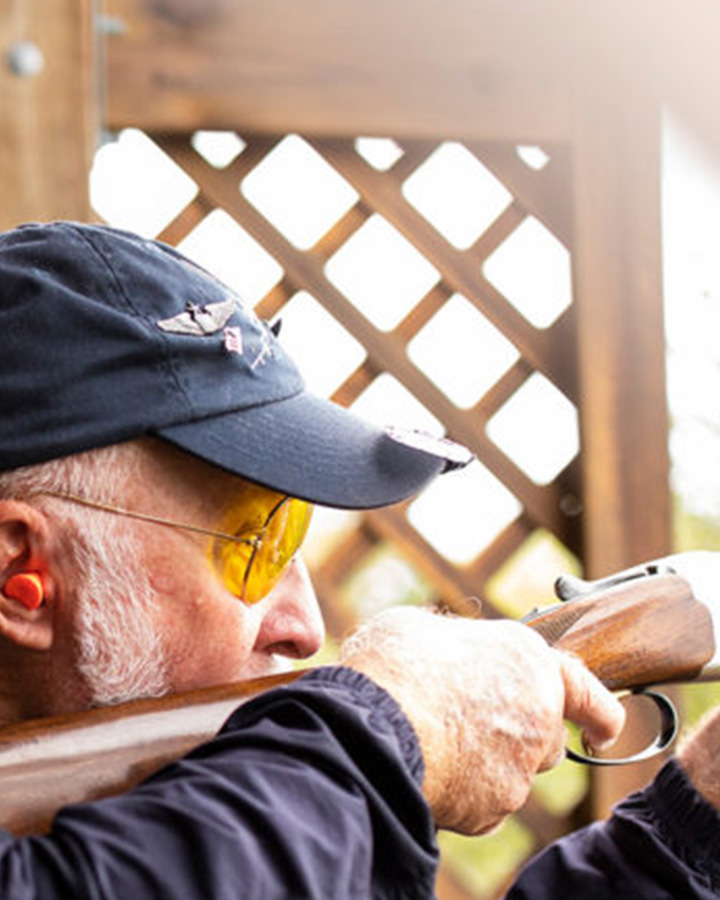 A Tom Klix event participant in a blue hat aims his shotgun.