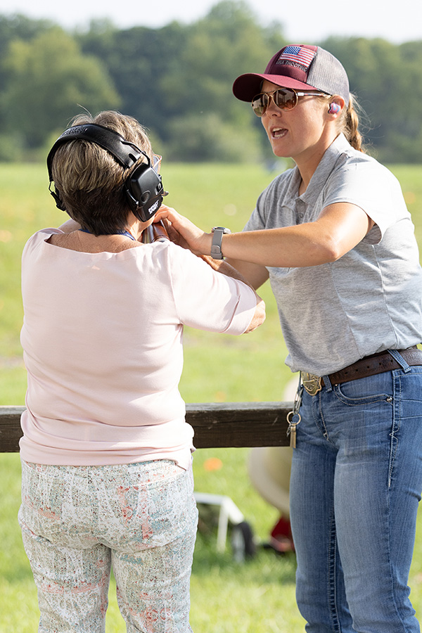 A Liberty Camps participant in a white shirt is instructed on shotgun use by a female coach.