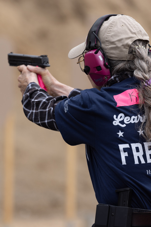 A Liberty Camp participant in a blue shirt and beige hat takes aim with her handgun.