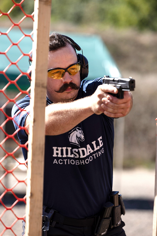 A Hillsdale student in a blue shirt displays a handgun.