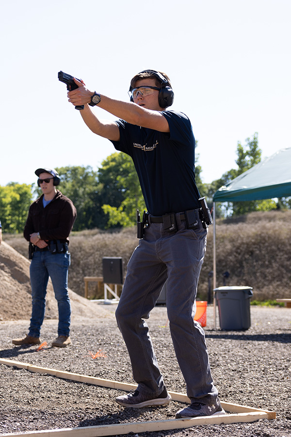 A young man stands with his feet apart taking the proper stance while practicing on the pistol range.