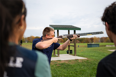 A firearm instructor aims a rifle.